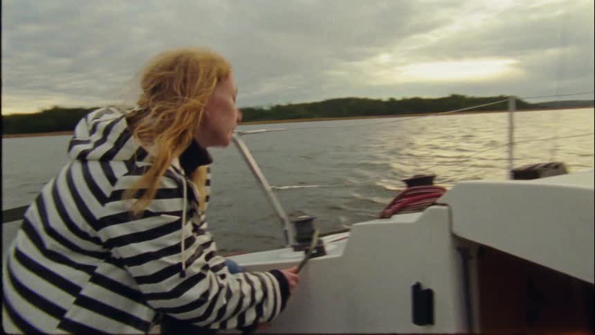 A young woman is driving a boat on a lake in the day time