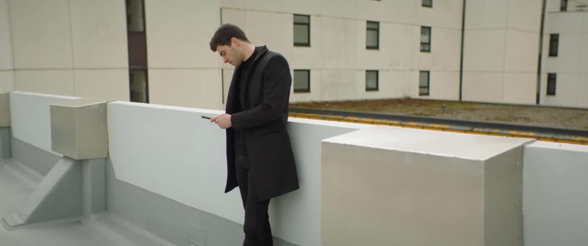 A man standing against a half wall looking at his phone