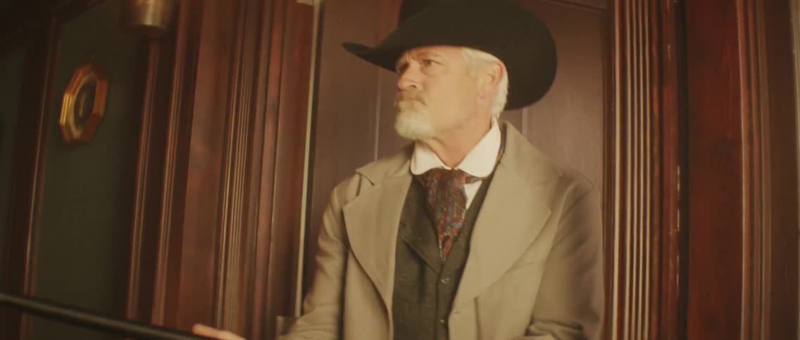 Man wearing western wear steps through door and shoots shotgun