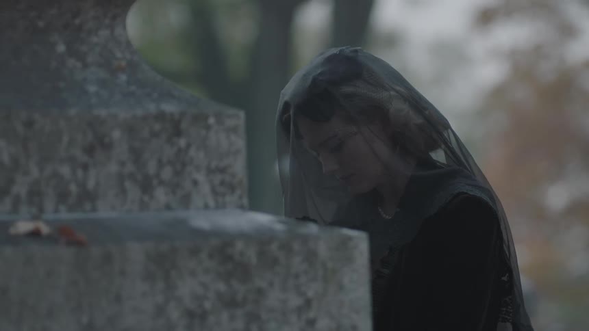A woman in a black veil sits at a gravestone