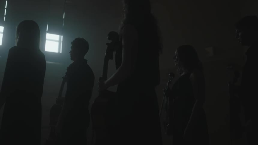 Musicians stand in a dim room