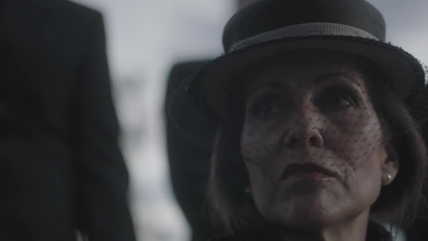 A woman wearing a hat with a veil looks to the side