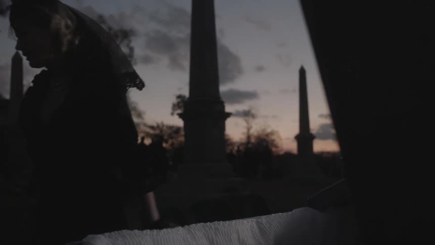 A woman mourns over an open casket in a cemetery