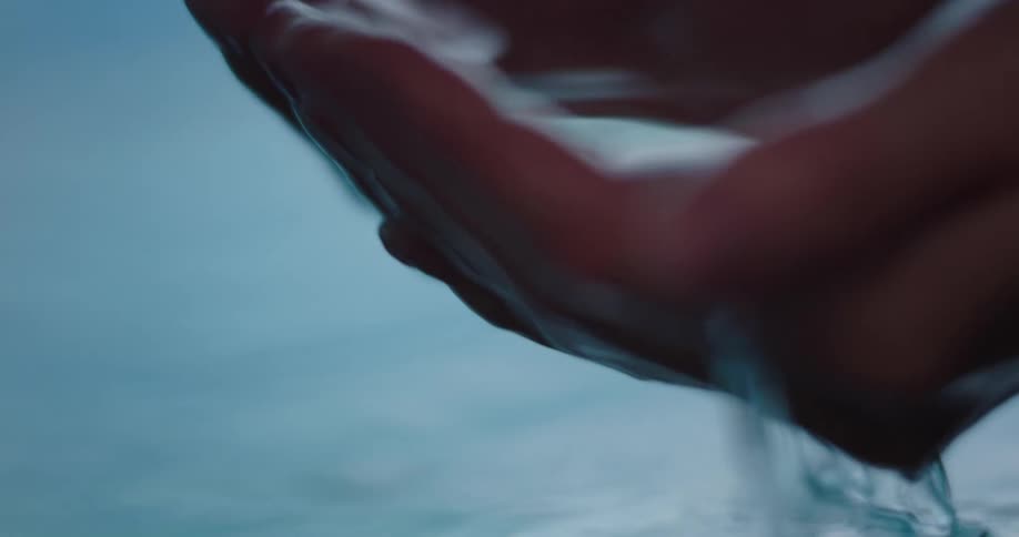 A woman dips her hands in pool water and cups them together