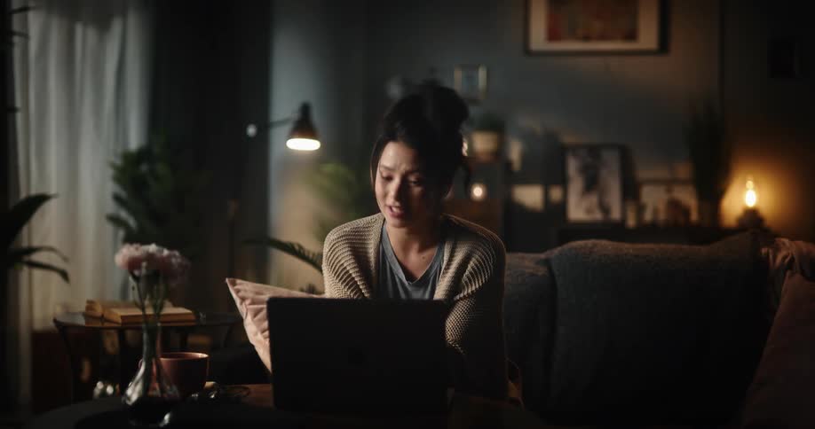 Woman talking on a laptop before closing it and leaning back into her couch satisfiyed