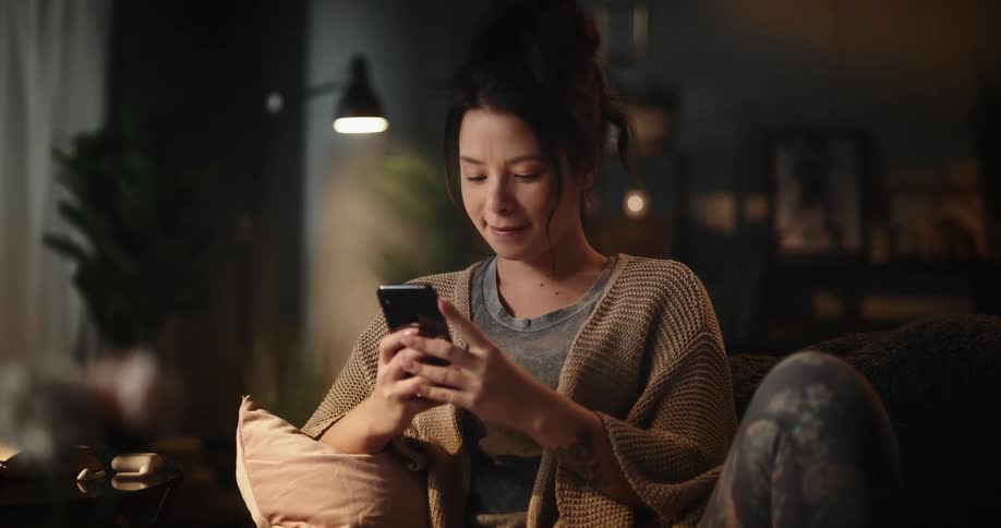 A woman texts on her phone while sitting on the couch