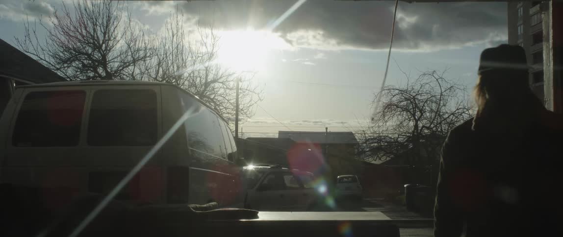 Silhouetted man pulls rope as he walks between parked van and building on sunny day