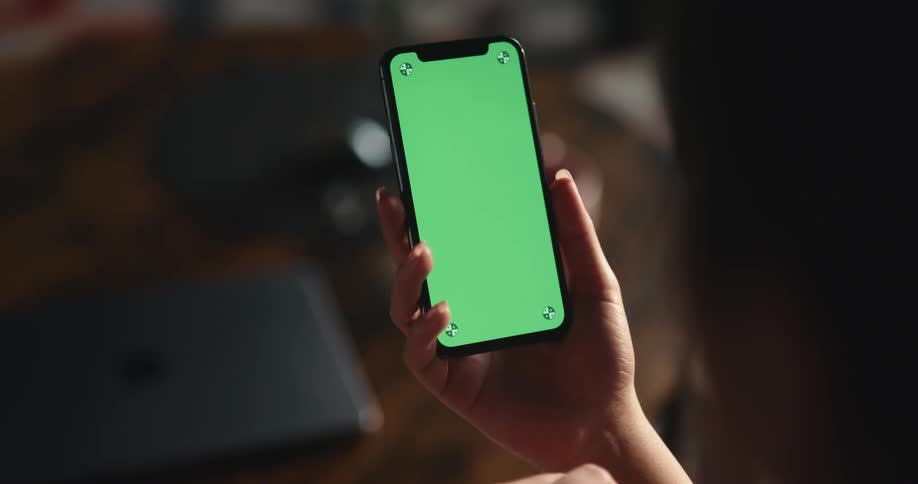 A woman is holding a cell phone with a green screen as she moves her finger across the surface