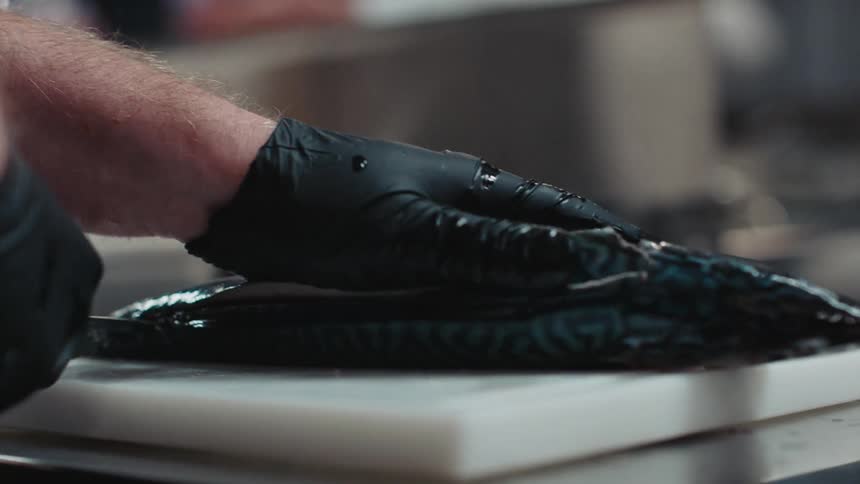Chef wearing black latex gloves uses a sharp kitchen knife to slice and cut a fish