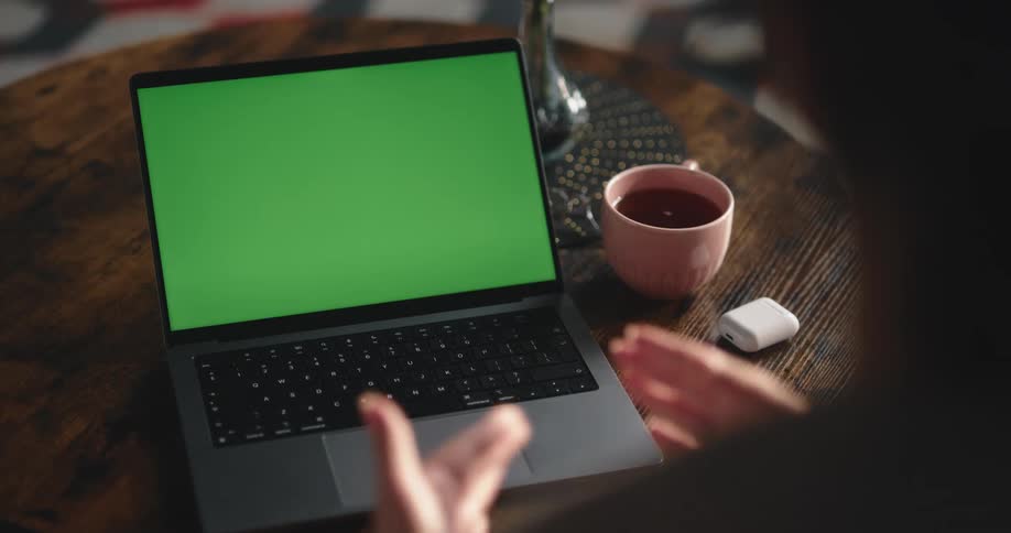 A woman gesturing to a laptop that has a green screen