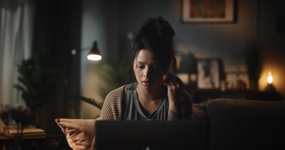 A young woman sitting down on a sofa to make a video call on a laptop