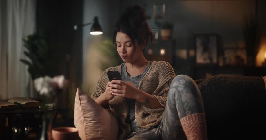 A woman is sitting in a chair texting on her phone