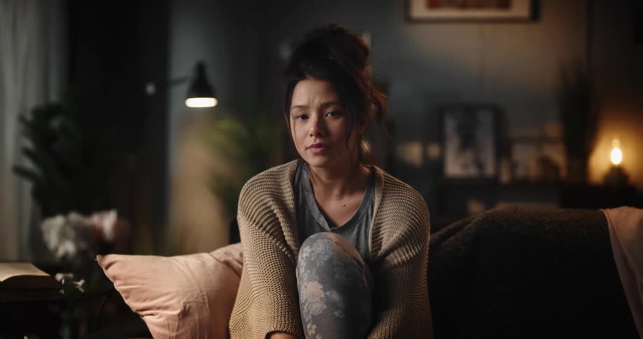 A woman is sitting on the couch with a very sad face as she cries
