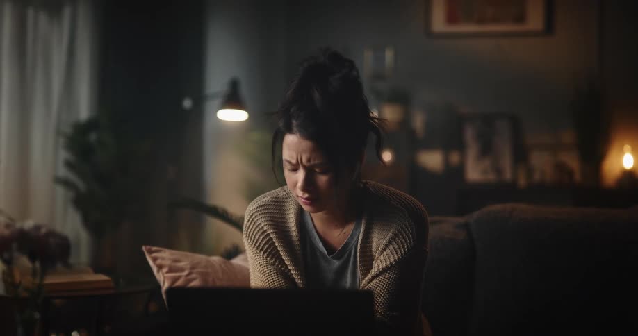 A sad looking woman sits at home and video chats on her laptop