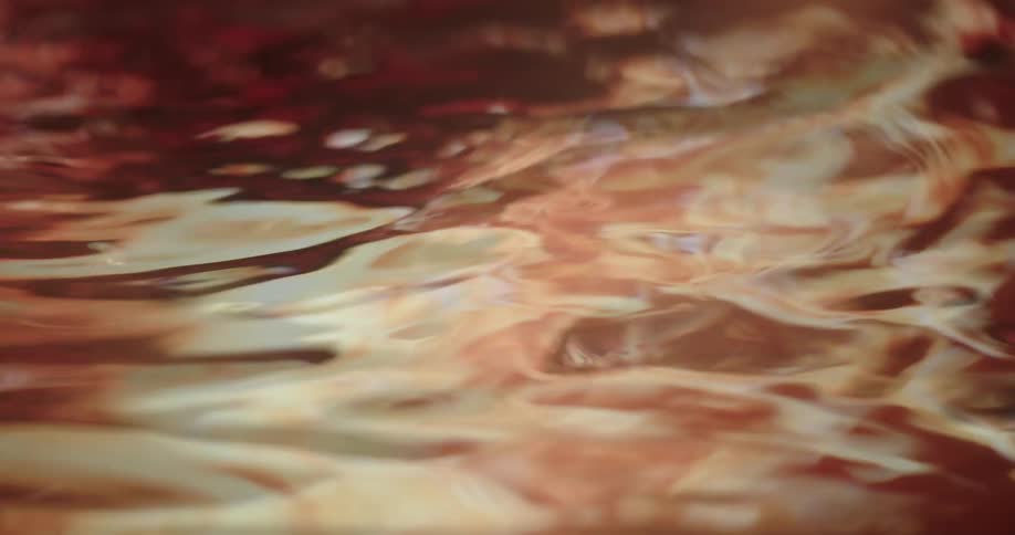 Ripples and waves move across surface of water reflecting red and orange colors of sunset