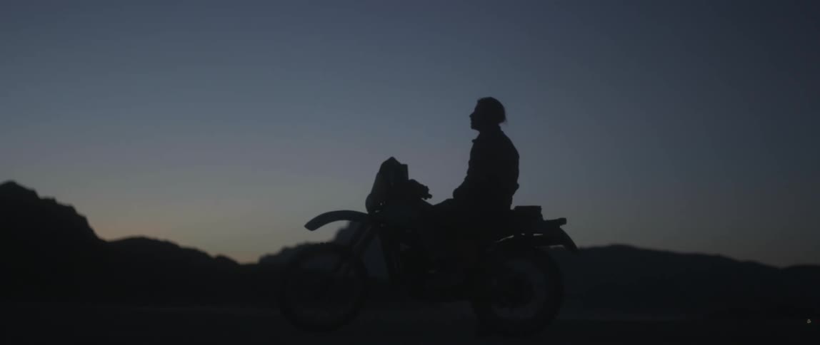 Silhouette of a man sitting on a motorcycle and there are mountains in the distance