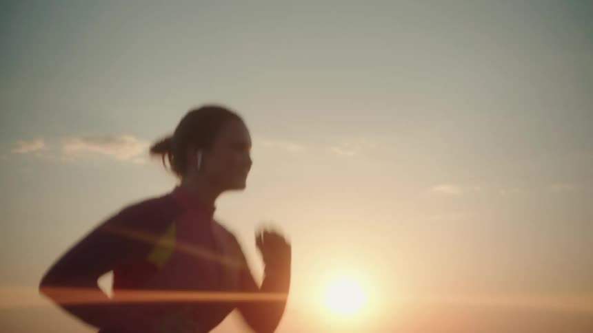 Silhouette of a young fit woman jogging next to the ocean at sunset