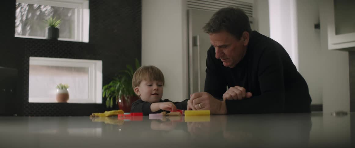 Father and son wearing black sweaters play with toys at kitchen island