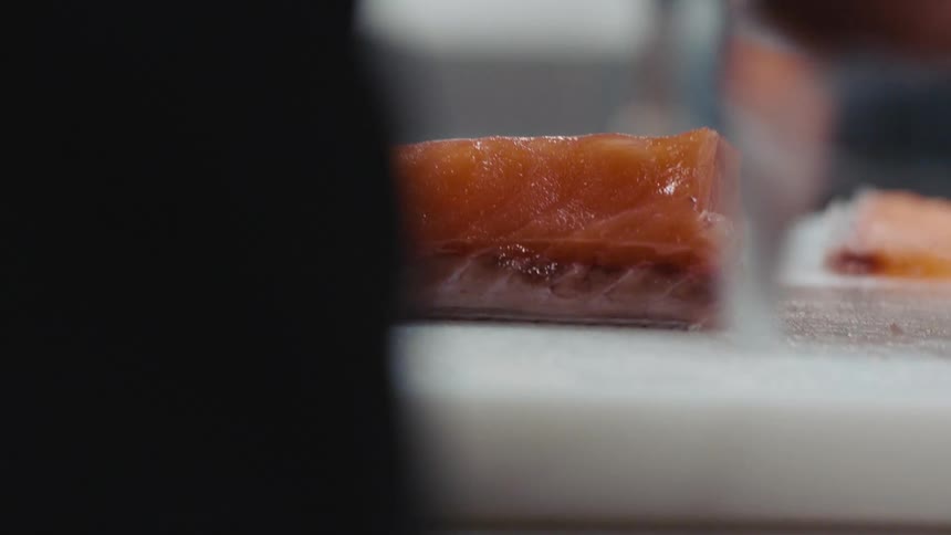 A chef is slicing thin pieces from a salmon filet and laying them aside