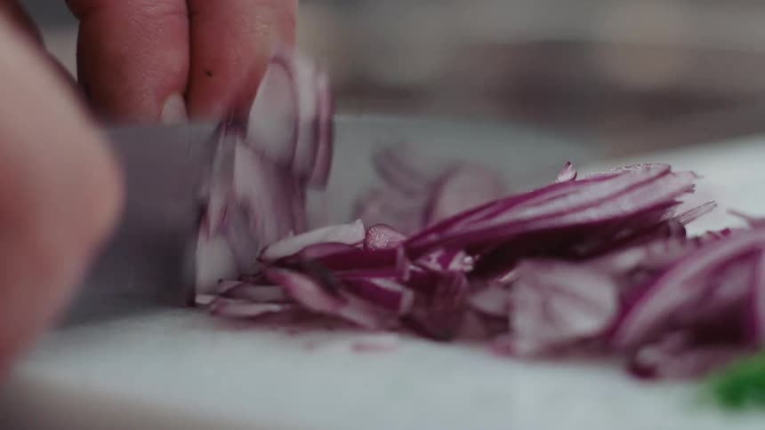 A man is slicing a red onion on a cutting board