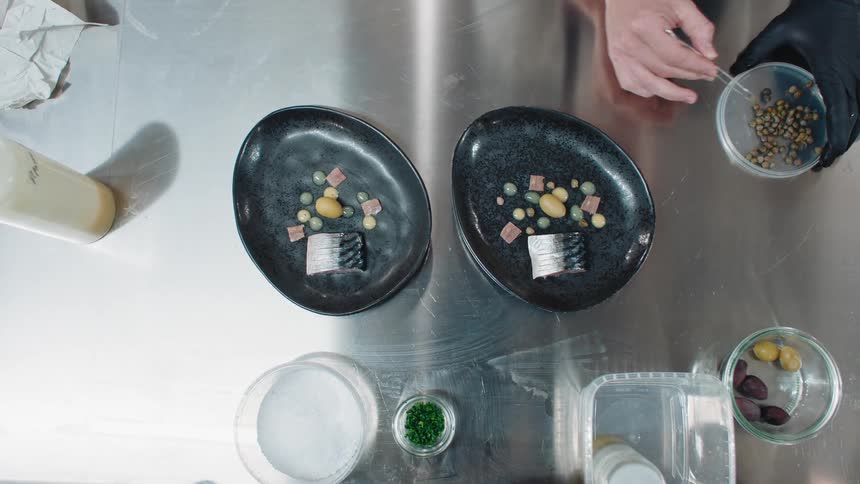 Man plates small beans onto two plates set on reflective metal surface