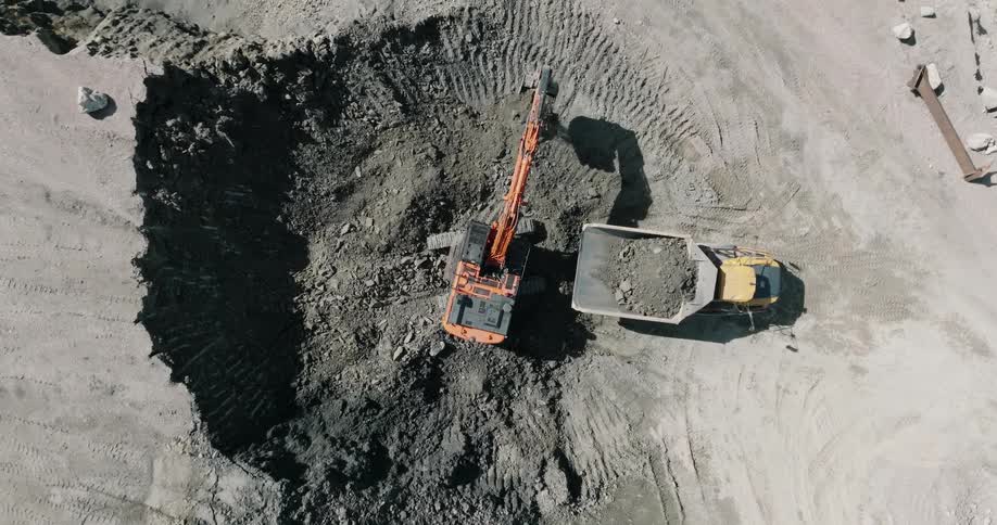 Construction crane digging hole in ground and lifting dirt into nearby dump truck