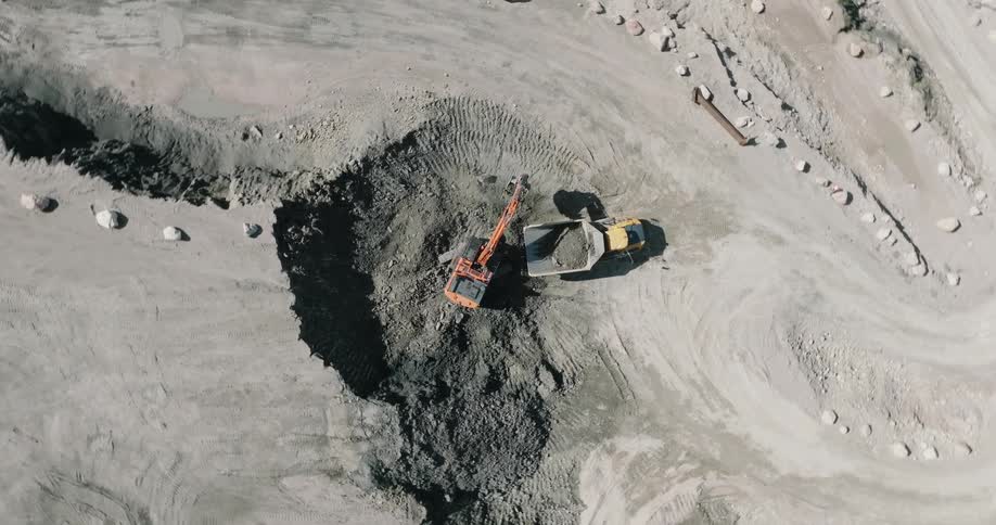 Aerial view of an excavator pouring gravel on the bed of a truck on a mine