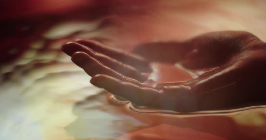 A persons hand emerging from water cupping it and creating ripples in the water