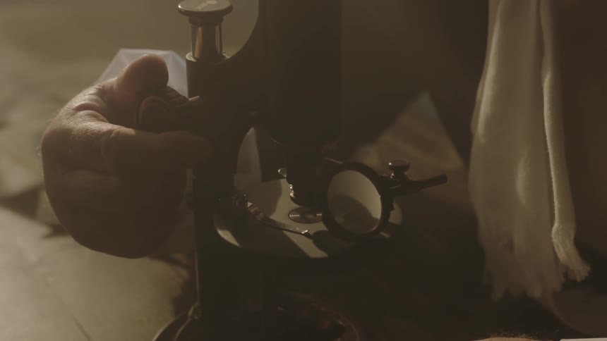 A hand adjusts a microscope