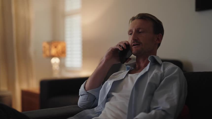 Man sitting on couch nods while talking on a smartphone