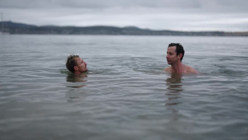 Large birds fly over men swimming in the ocean