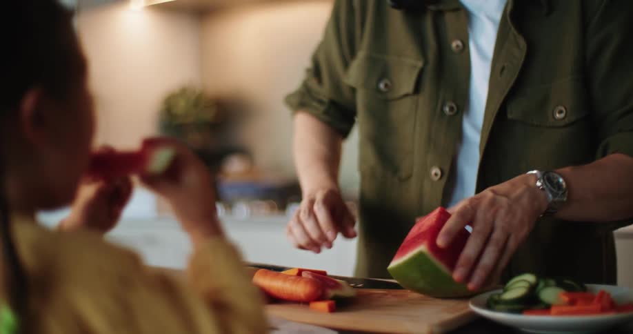 A man hands his daughter sliced watermelon while talking on the phone