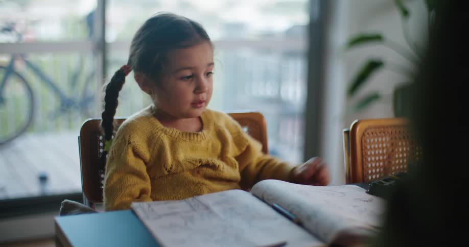 Daughter with braids and yellow sweater sits at table talking to dad