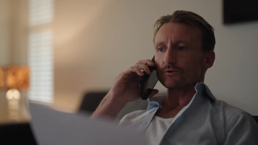 A man is talking on his phone as he holds a document