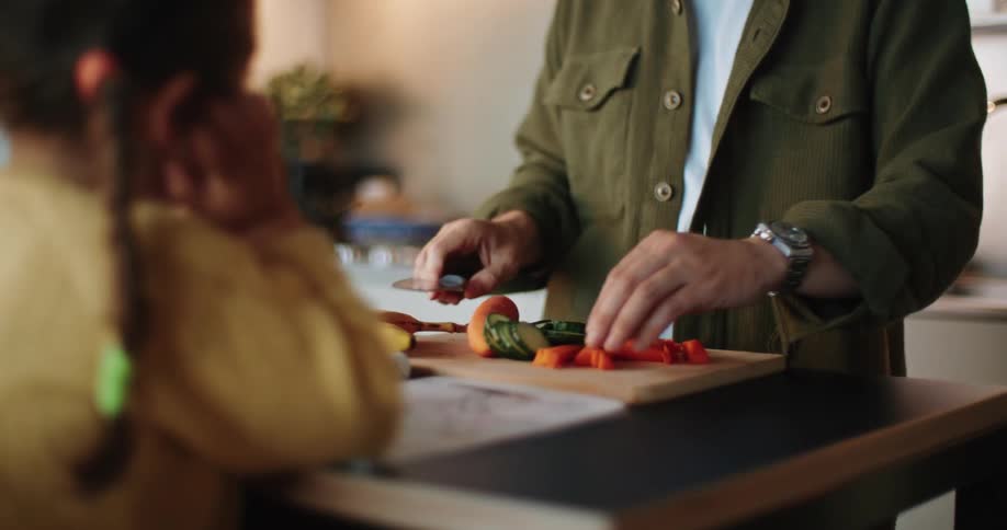 Father and daughter eat slices of carrots while preparing a meal in the kitchen at home