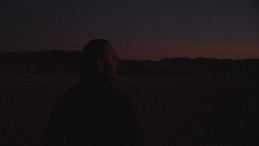 Silhouette of the back and head of a man walking on a desert at nightfall