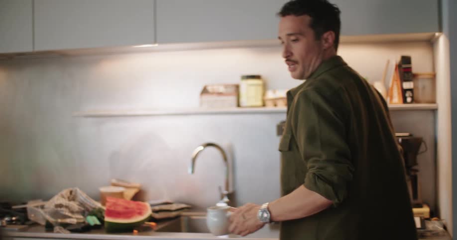 A man pours himself a mug of hot water after cutting watermelon
