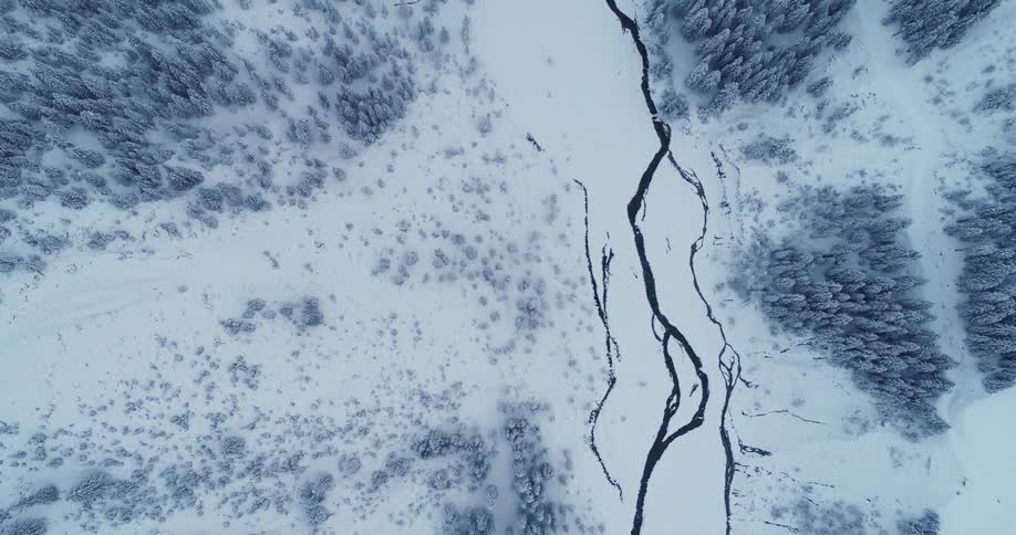 River flows through snow covered area between conifer forests
