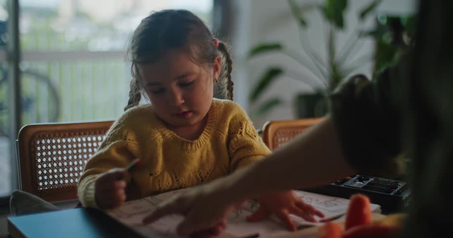 Father chops vegetables after giving crayon to daughter coloring across table from him