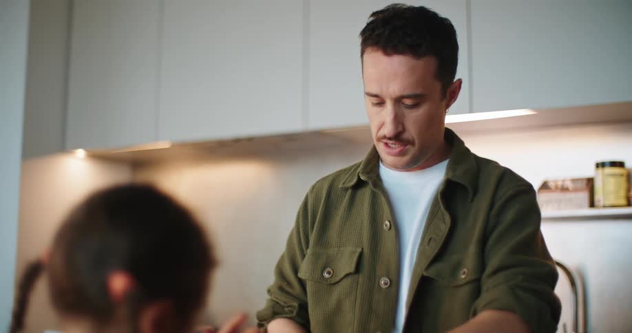 Man makes a meal in kitchen while he talks to sitting daughter