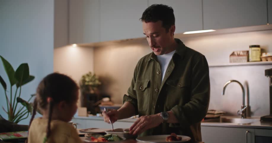 Father talks and high fives daughter while serving food onto plate in kitchen
