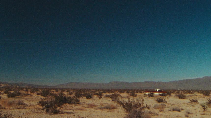 A truck driving through the desert with a blue sky and mountains in the distance