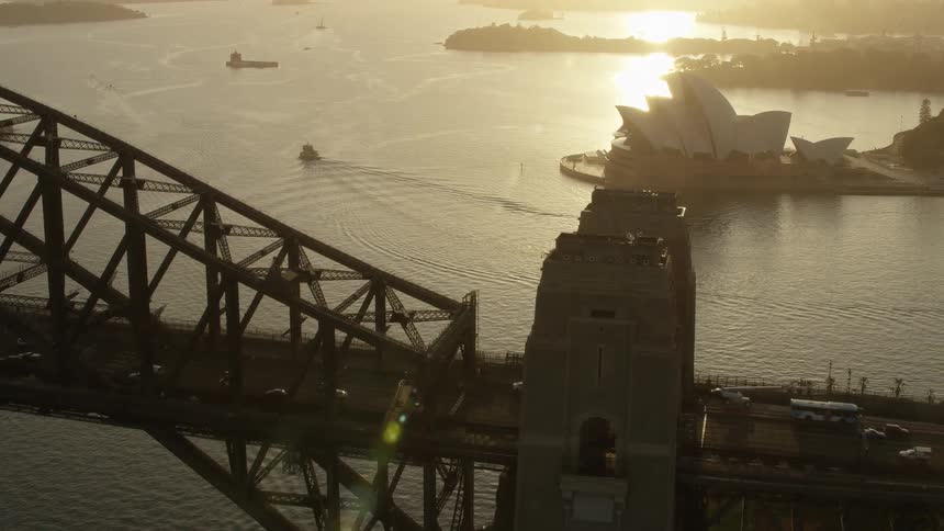 An aerial of a bridge with cars traveling and a body of water with boats in the back