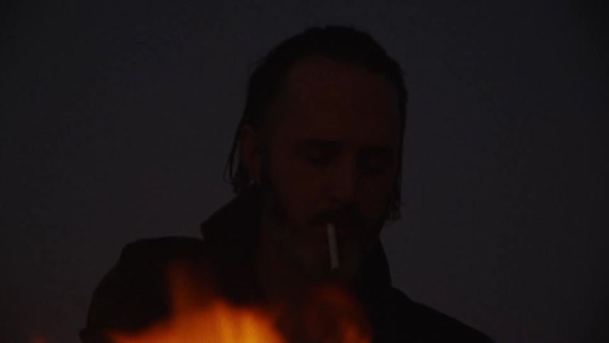 A flame burning in front of a persons silhouette at night