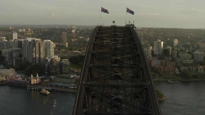 An aerial orbiting view of a large bridge over a citys waterway at dusk