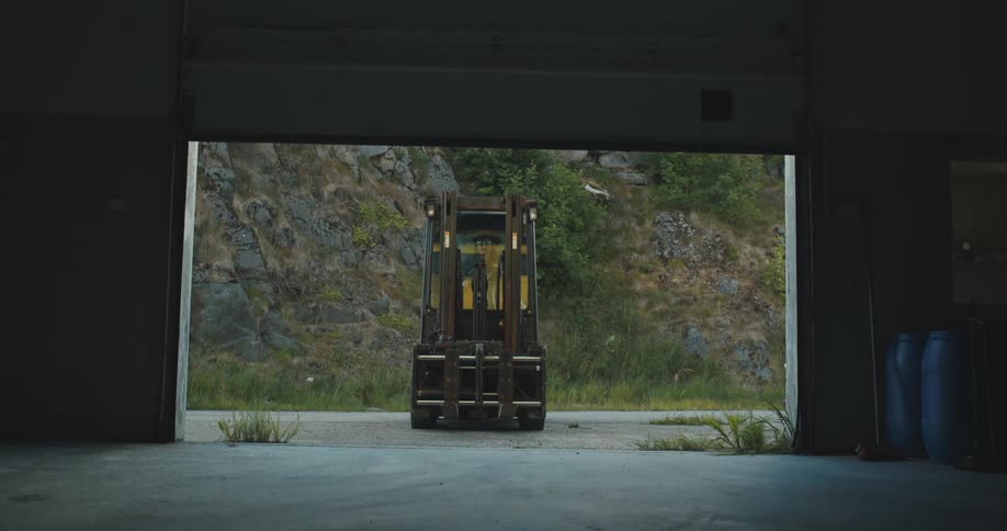 An operator drives a forklift into a building after a large garage door opens