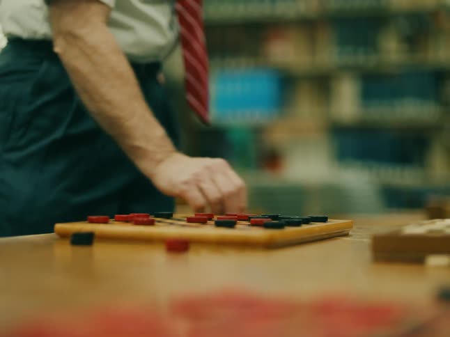 A lone man wearing a red tie moves the pieces of a game of checkers