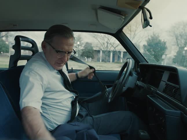 A man parks his car undoes his seat belt and grabs his jacket and suitcase