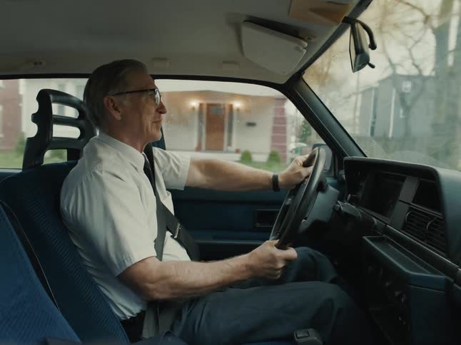 An older man driving a car through a suburban neighborhood