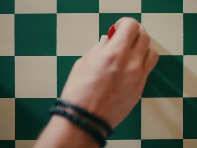 A red game piece being moved on a checkered board by someones finger